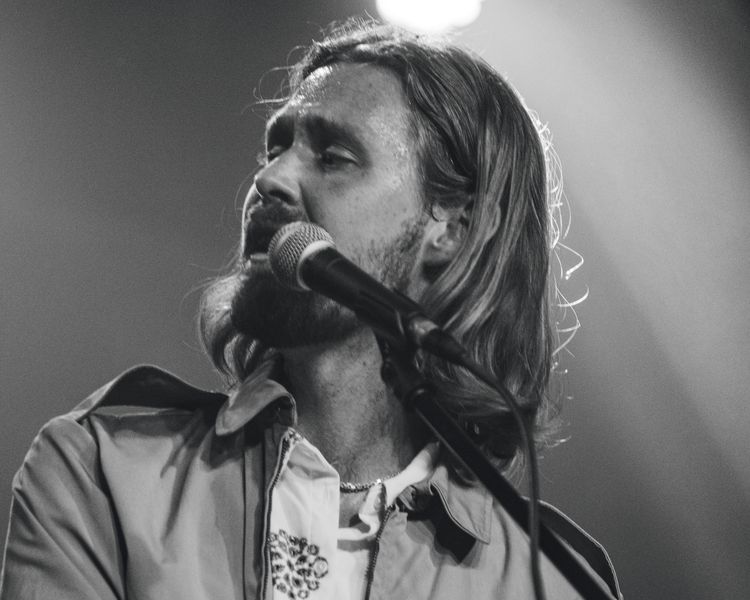 Tobias Lund singing into the mic at the keys under a stage light, in black and white